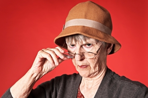 Old woman looks disapprovingly over spectacles at camera